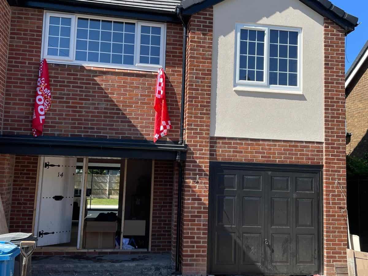 Modern two-storey house with brick and white exterior, large windows, and a black garage door.