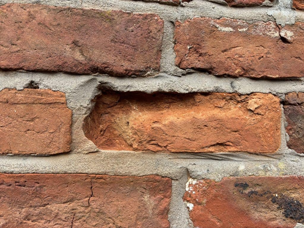Close-up of a brick wall with a damaged brick and mortar.